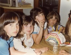 Annoyed preteen girls surrounding rainbow cake.