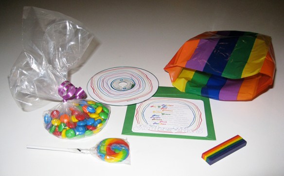 goody bag items for a rainbow-themed party, including m&ms, lollipop, mix music CD, rainbow crayon, and rainbow striped bag.