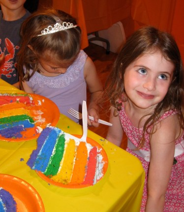 Happy girl with a huge hunk of rainbow cake in front of her.